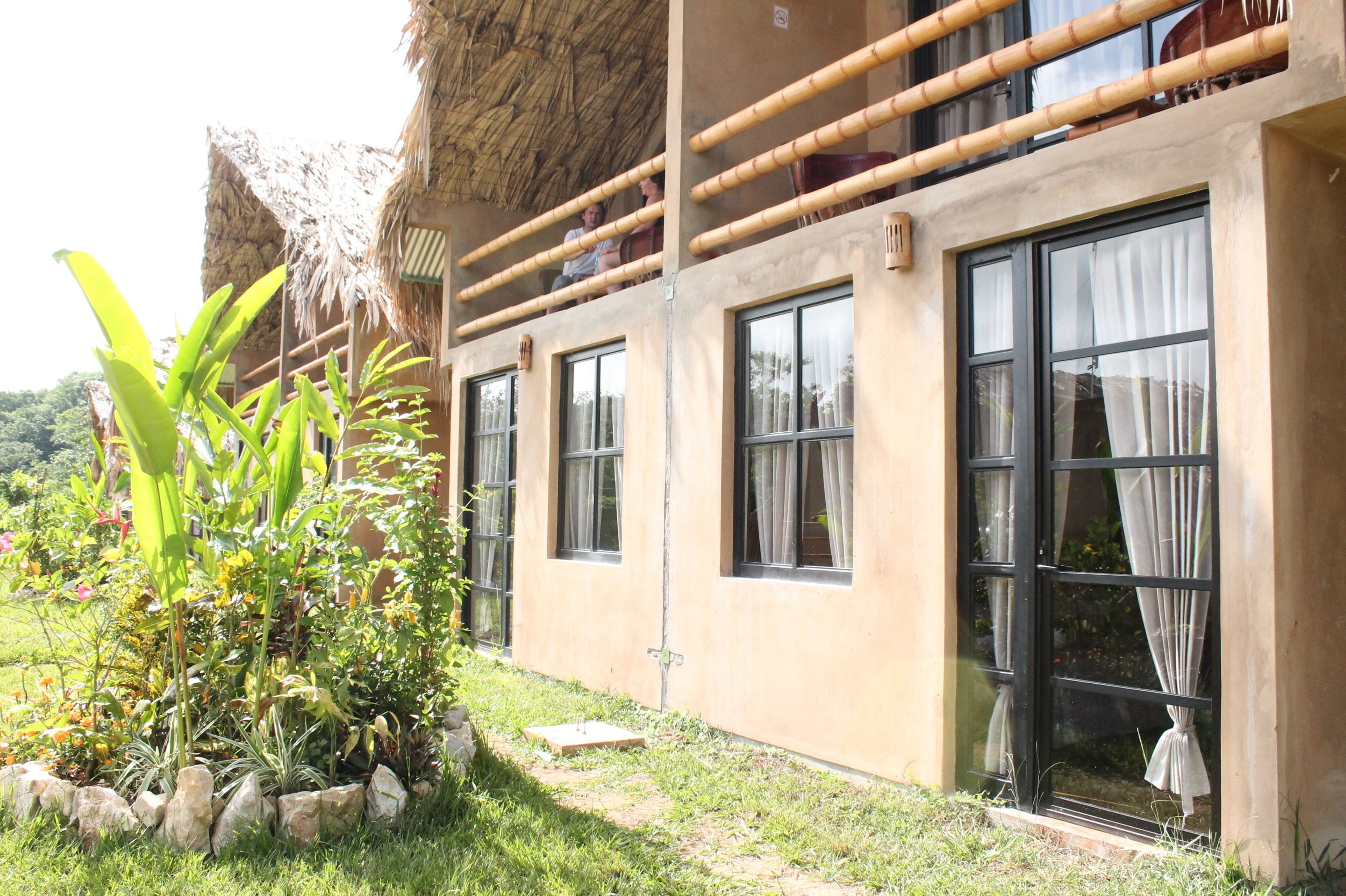 A building with large windows, a thatched roof, and a garden with tropical plants.