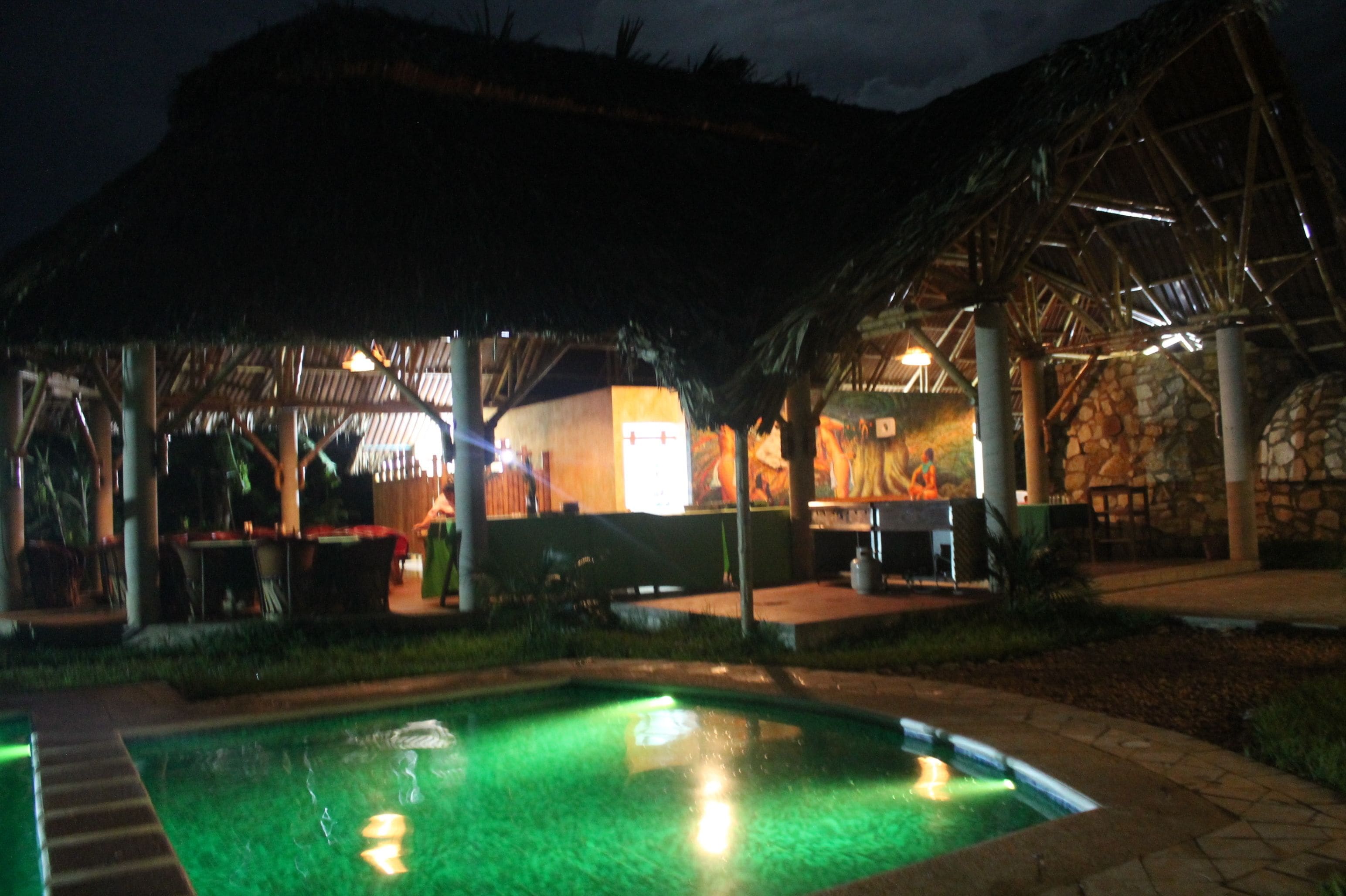 A nighttime view of a resort with a swimming pool, outdoor seating, and a covered dining area.