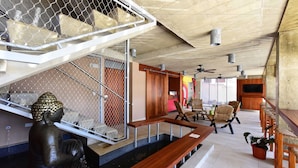 A modern interior with a Buddha statue in a water feature, wooden seating, and a staircase with a metal railing. - Dream Inn PR (San Juan)