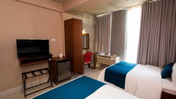 A hotel room with a bed, a desk, a television, and a window with curtains.