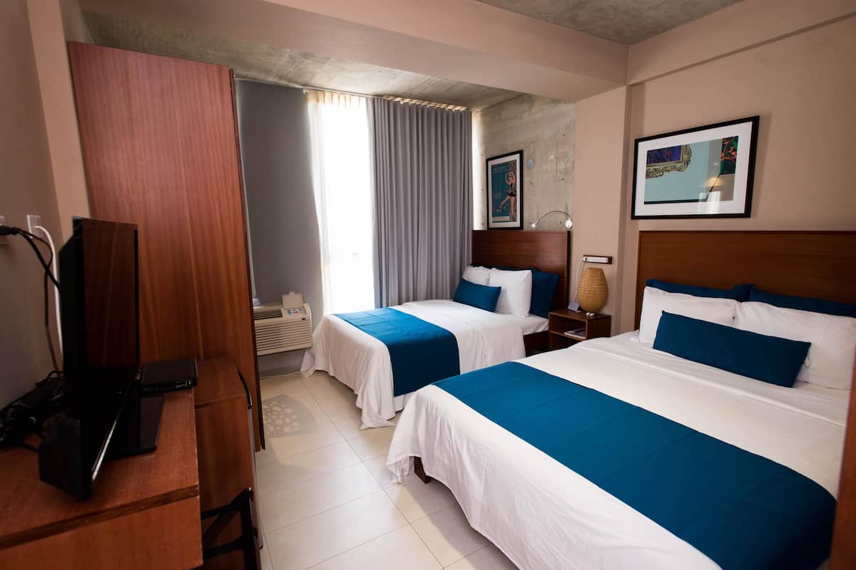 Ein Hotelzimmer mit zwei Betten, einem Schreibtisch, einem Laptop, einer Lampe und einem gerahmten Bild an der Wand.