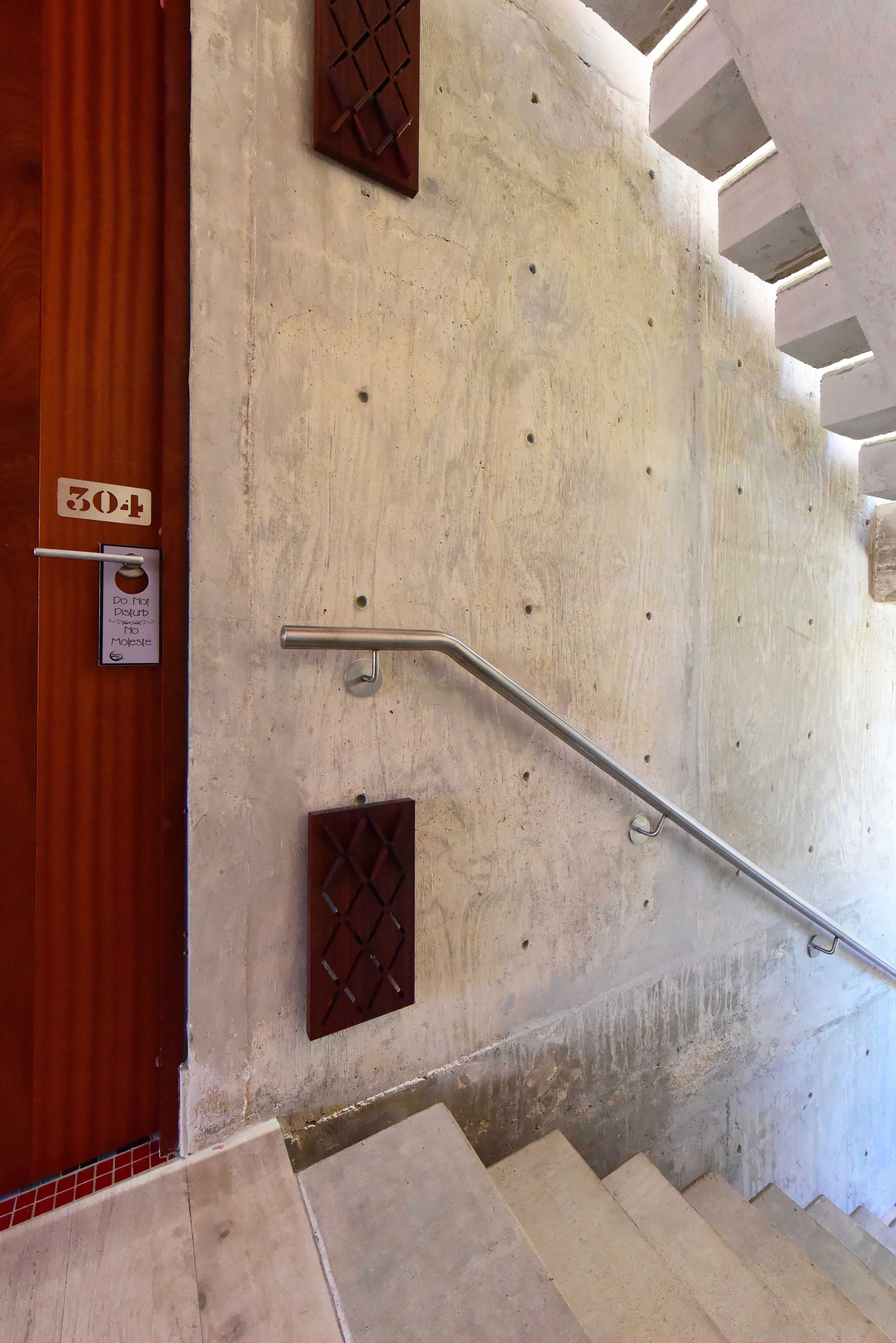 Escada de concreto com corrimãos de metal, porta de madeira com placa de número e aviso de 'Não Perturbe'.
