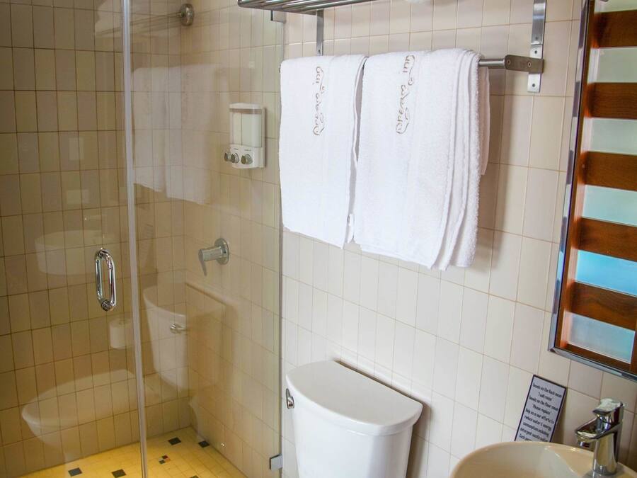A bathroom with a glass-enclosed shower, a white toilet, a red sink, and white towels on a rack.