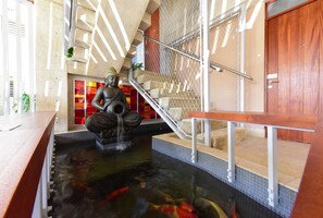 Un bassin à carpes koï, une statue de Bouddha, un banc en bois et un escalier avec une rampe en métal.