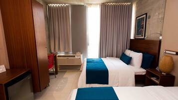 A hotel room with two beds, a desk, a chair, a heater, and a lamp.