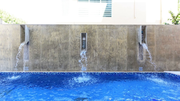 A swimming pool with water flowing from a concrete wall into the pool. - Dream Inn PR (San Juan)