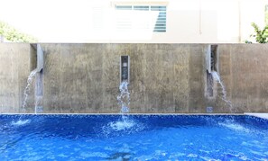 A swimming pool with water flowing from a concrete wall into the pool. - Dream Inn PR (San Juan)