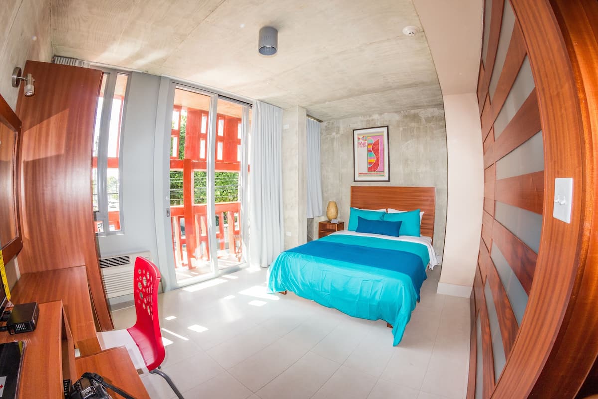 Ein Hotelzimmer mit einem großen Bett, einem Schreibtisch mit Stuhl und Blick ins Freie.