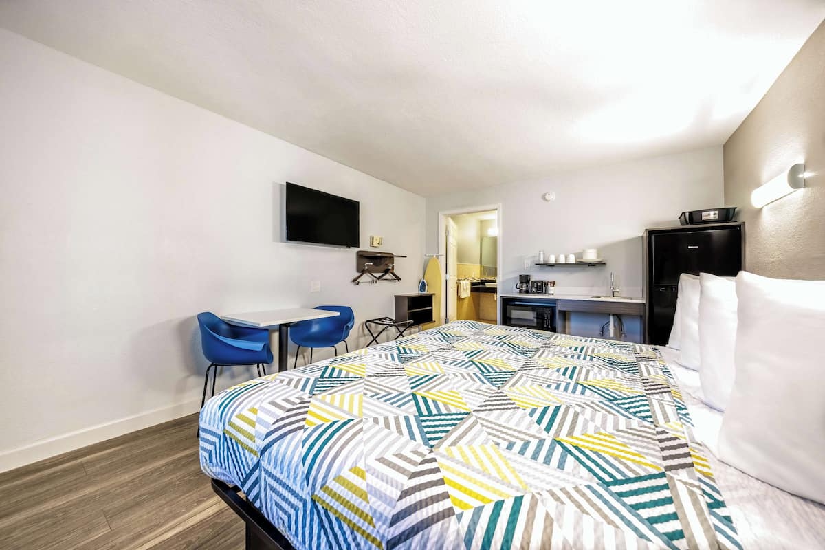 A hotel room with a bed, a desk, a chair, a television, and a kitchenette.