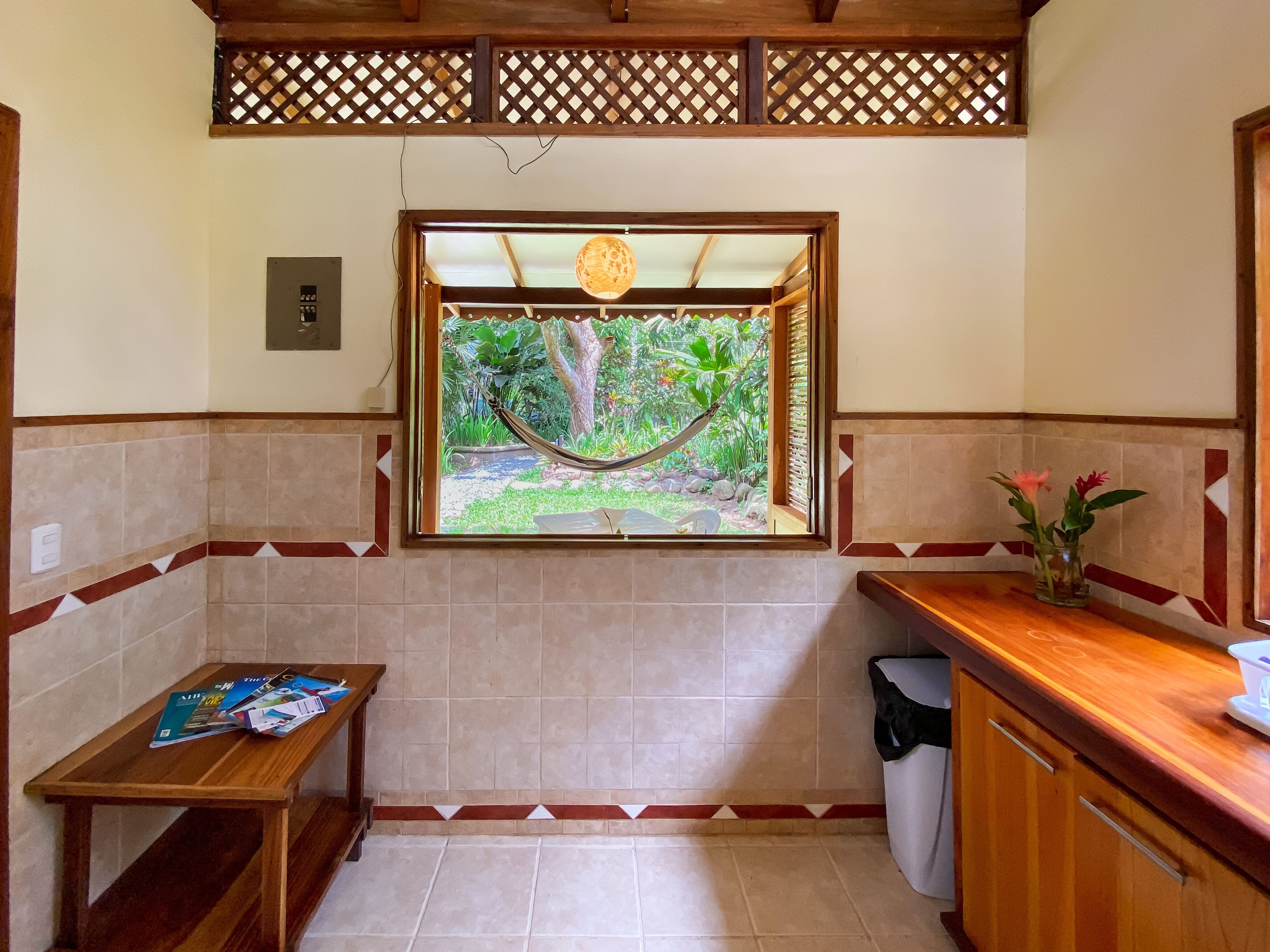 Una cocina compacta con ventana a un jardín, una mesa de madera con revistas y un cubo de basura.