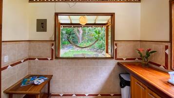 Una cocina compacta con ventana a un jardín, una mesa de madera con revistas y un cubo de basura.