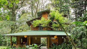 A wooden cabin with a green roof, surrounded by lush greenery and trees. - La Finca Chica (Cahuita)
