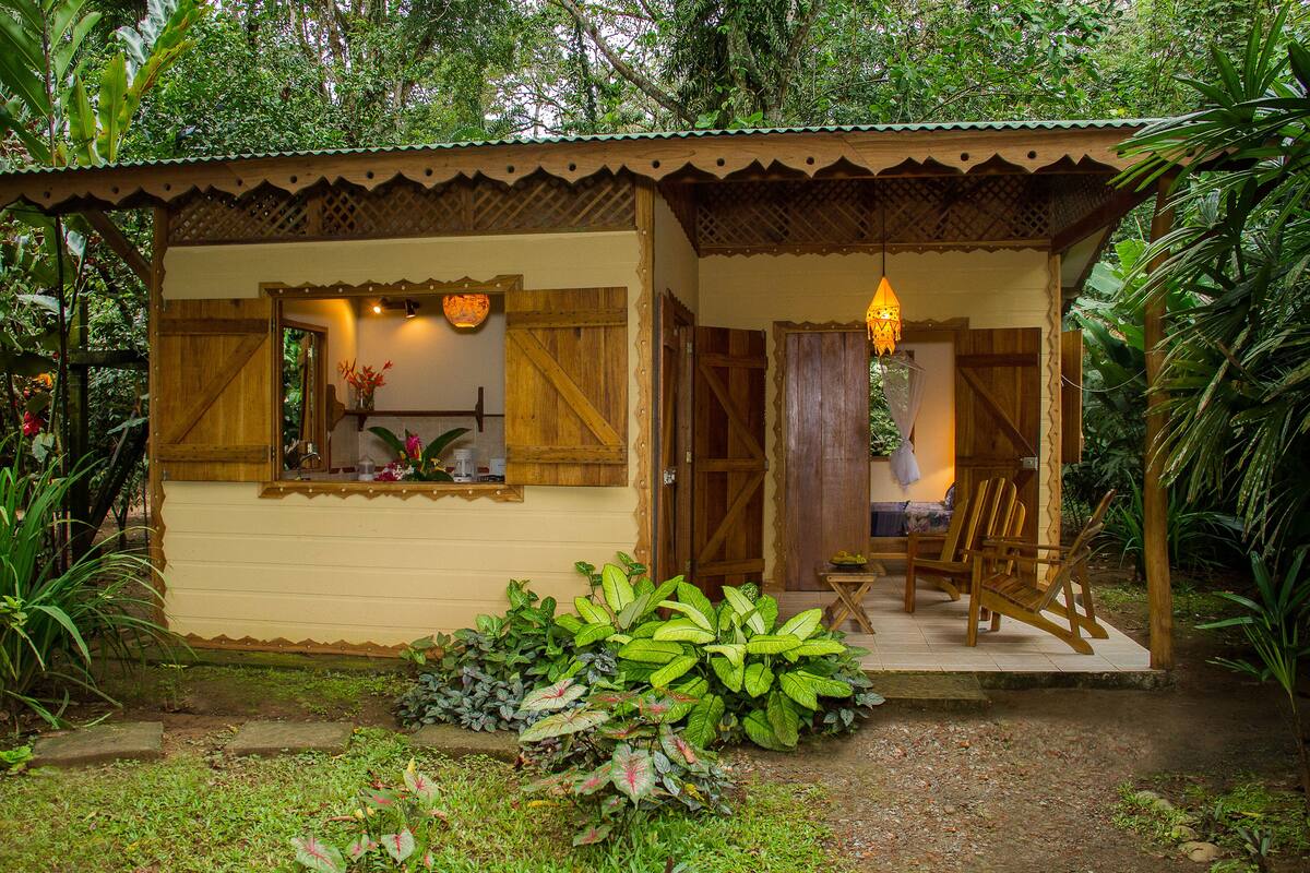 Ein kleines Holzhaus mit Veranda, umgeben von üppigem Grün.
