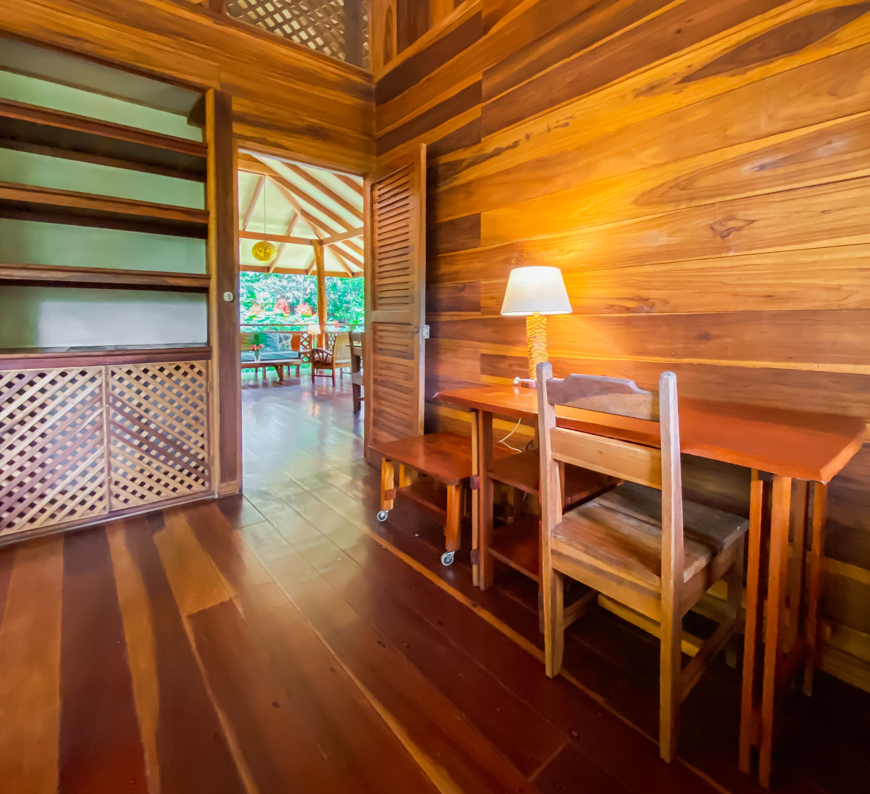 A wooden interior with a table and chairs, a lamp, and a view of an outdoor area.