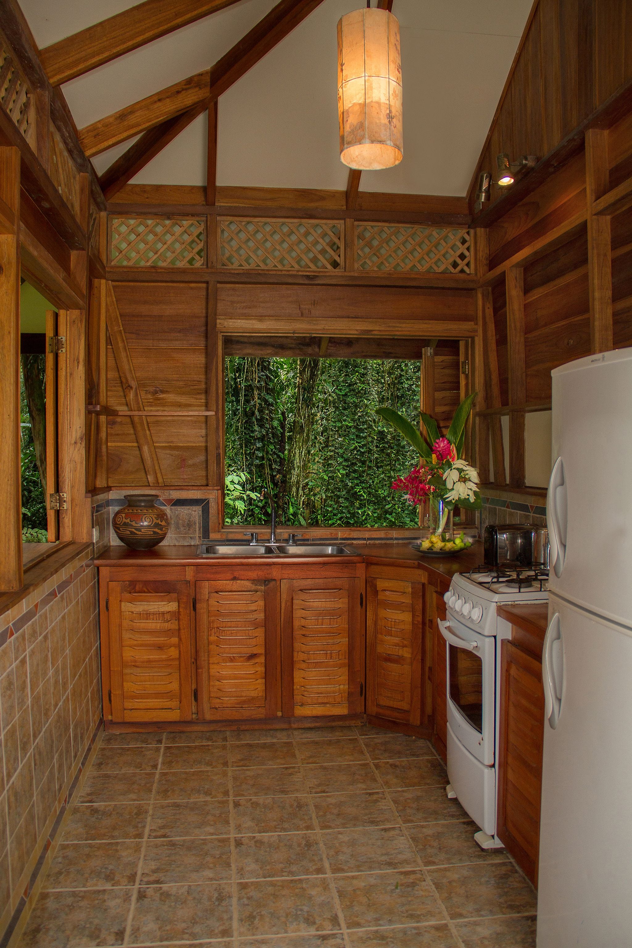 Une cuisine avec des meubles de rangement en bois, une cuisinière, un évier et une fenêtre donnant sur un paysage verdoyant.