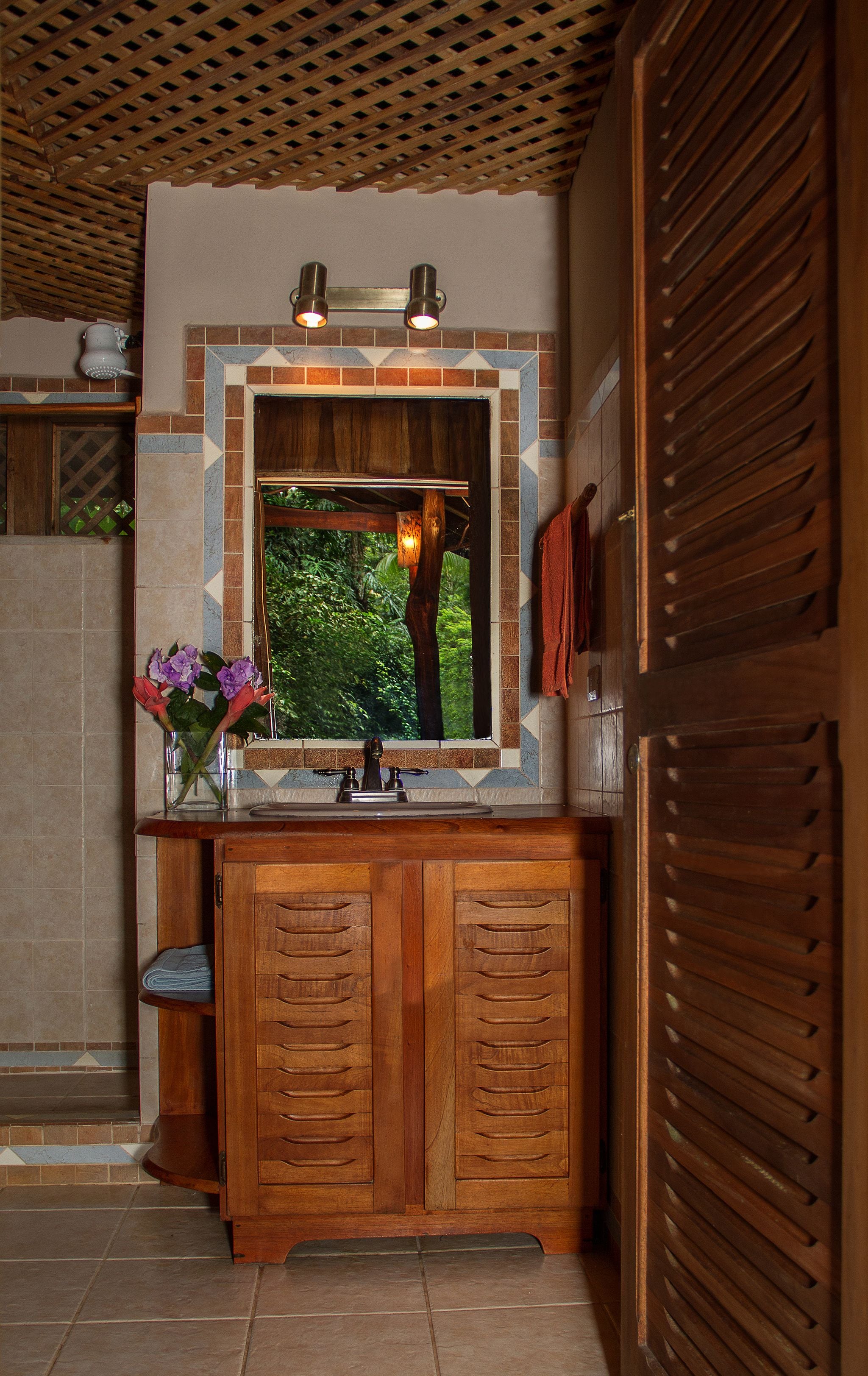 A wooden vanity with a built-in sink, a mirror, and a window with a view of greenery.