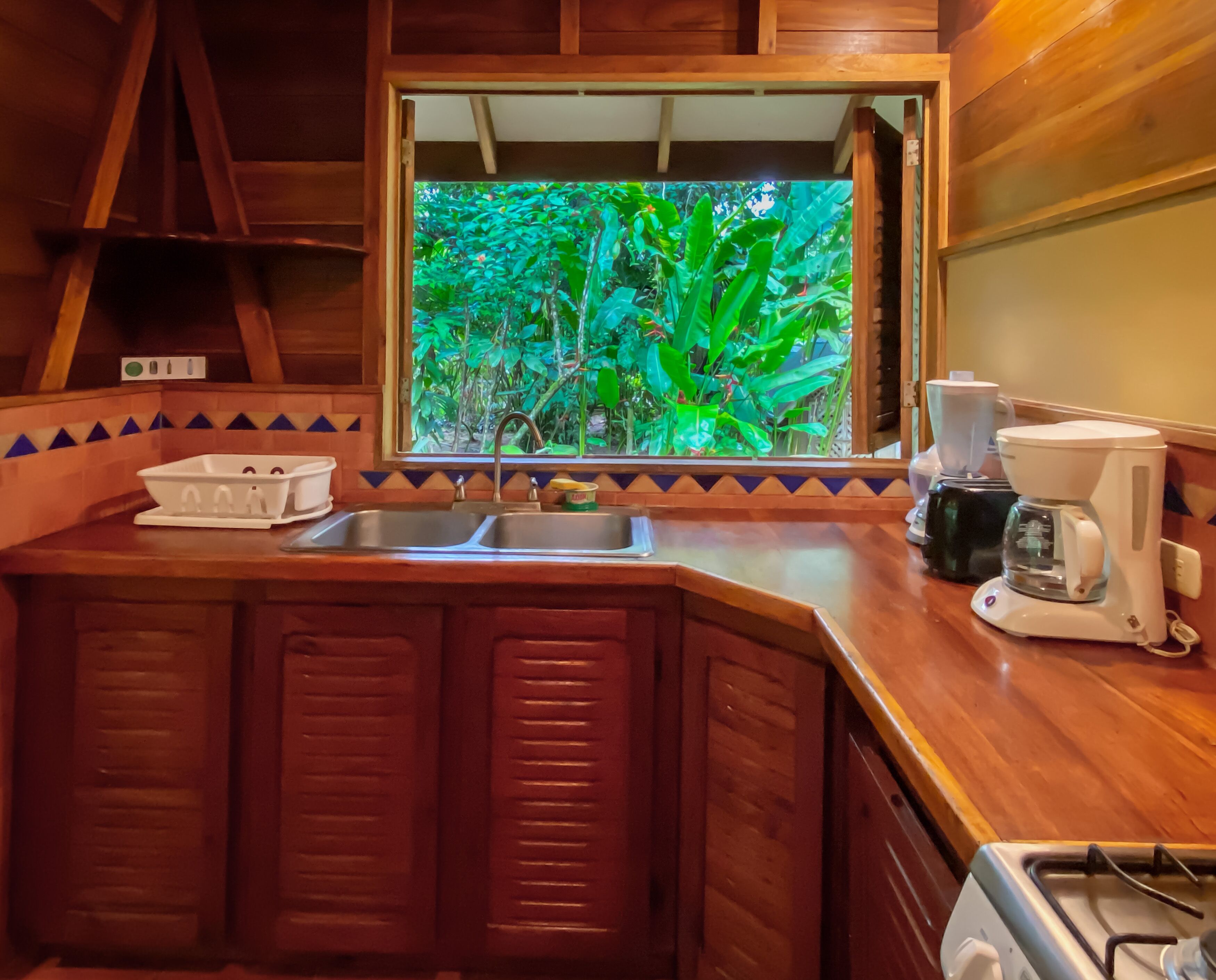 A kitchen with wooden cabinets, a window with a view of greenery, a coffee maker, and a sink.