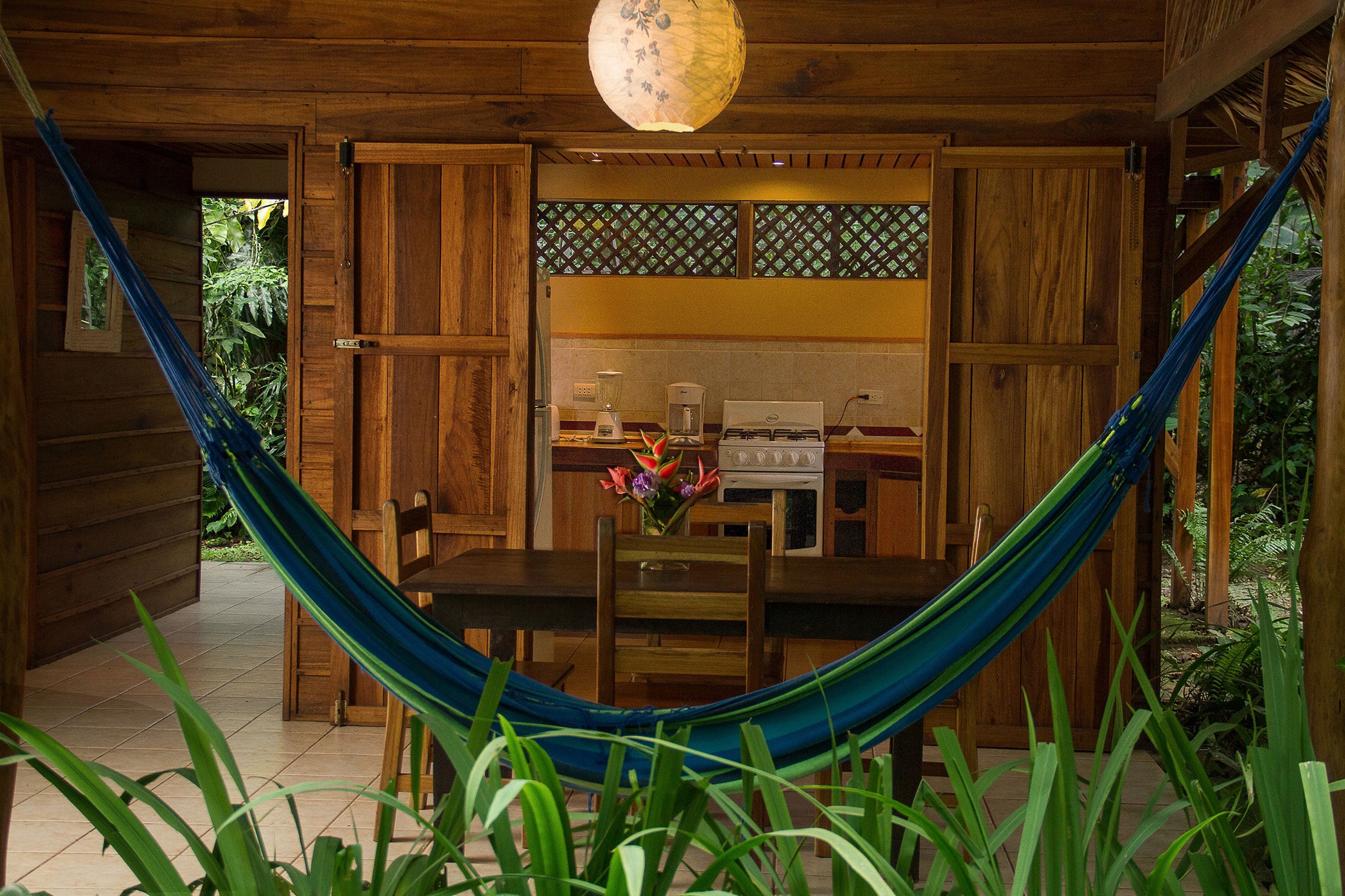 A wooden kitchen with a dining table, chairs, and a hammock.
