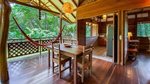 A wooden deck with a table and chairs, a hammock, and a view of lush greenery. - La Finca Chica (Cahuita)