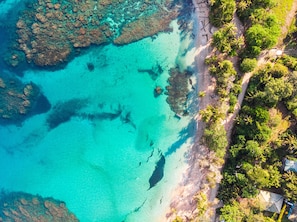 An aerial view of a coastal area with clear turquoise waters, a sandy beach, and dense tropical vegetation. - La Finca Chica (Cahuita)