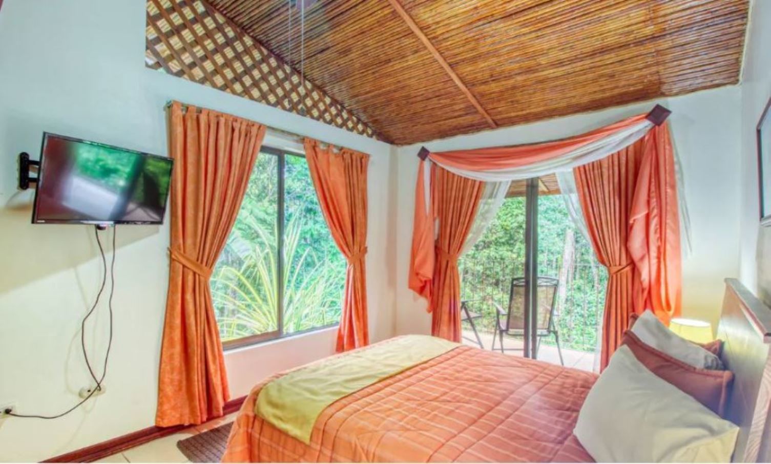A bedroom with a bed, a TV mounted on the wall, and windows with curtains.