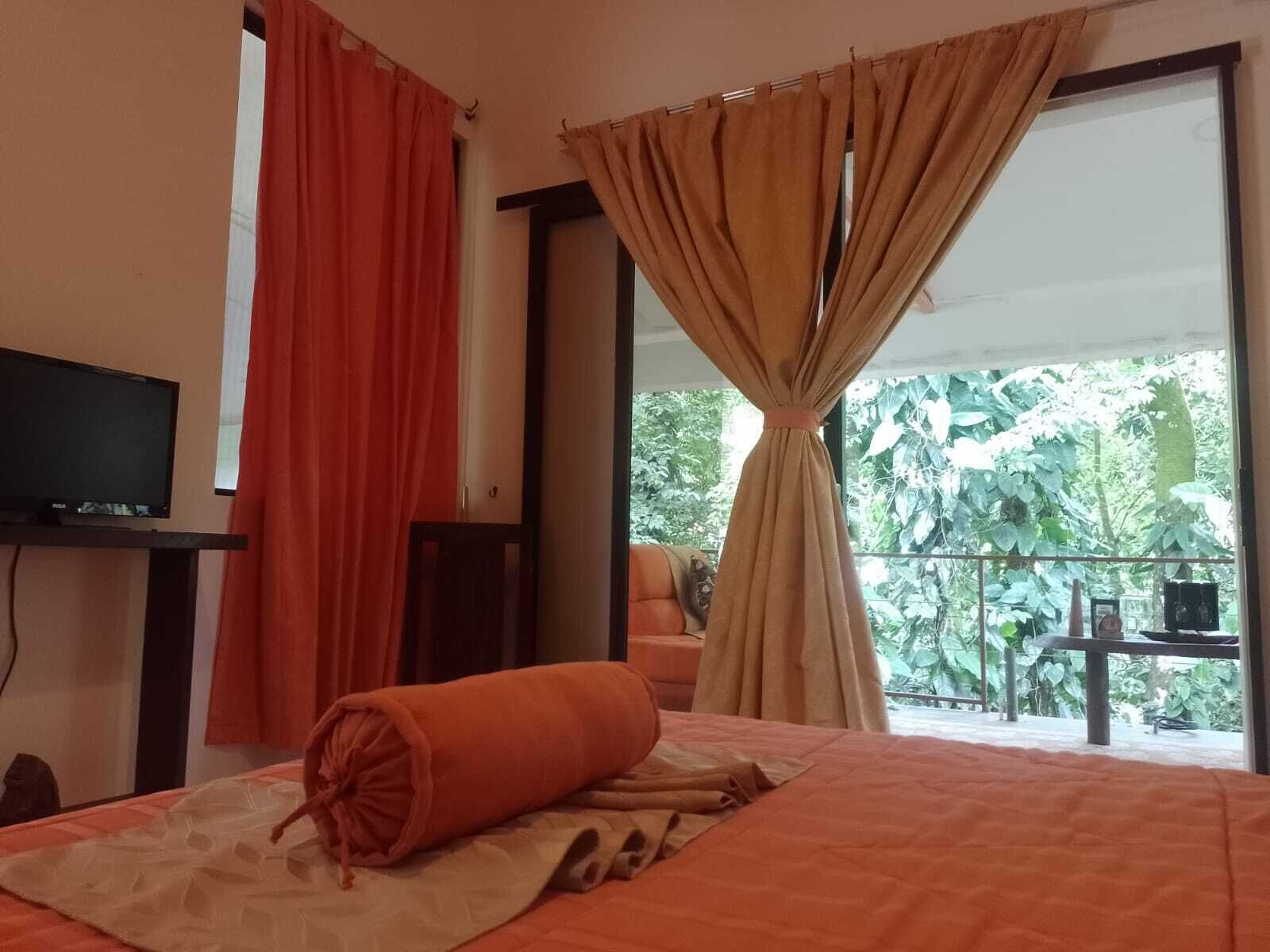A hotel room with a bed, a television, and a balcony with curtains.