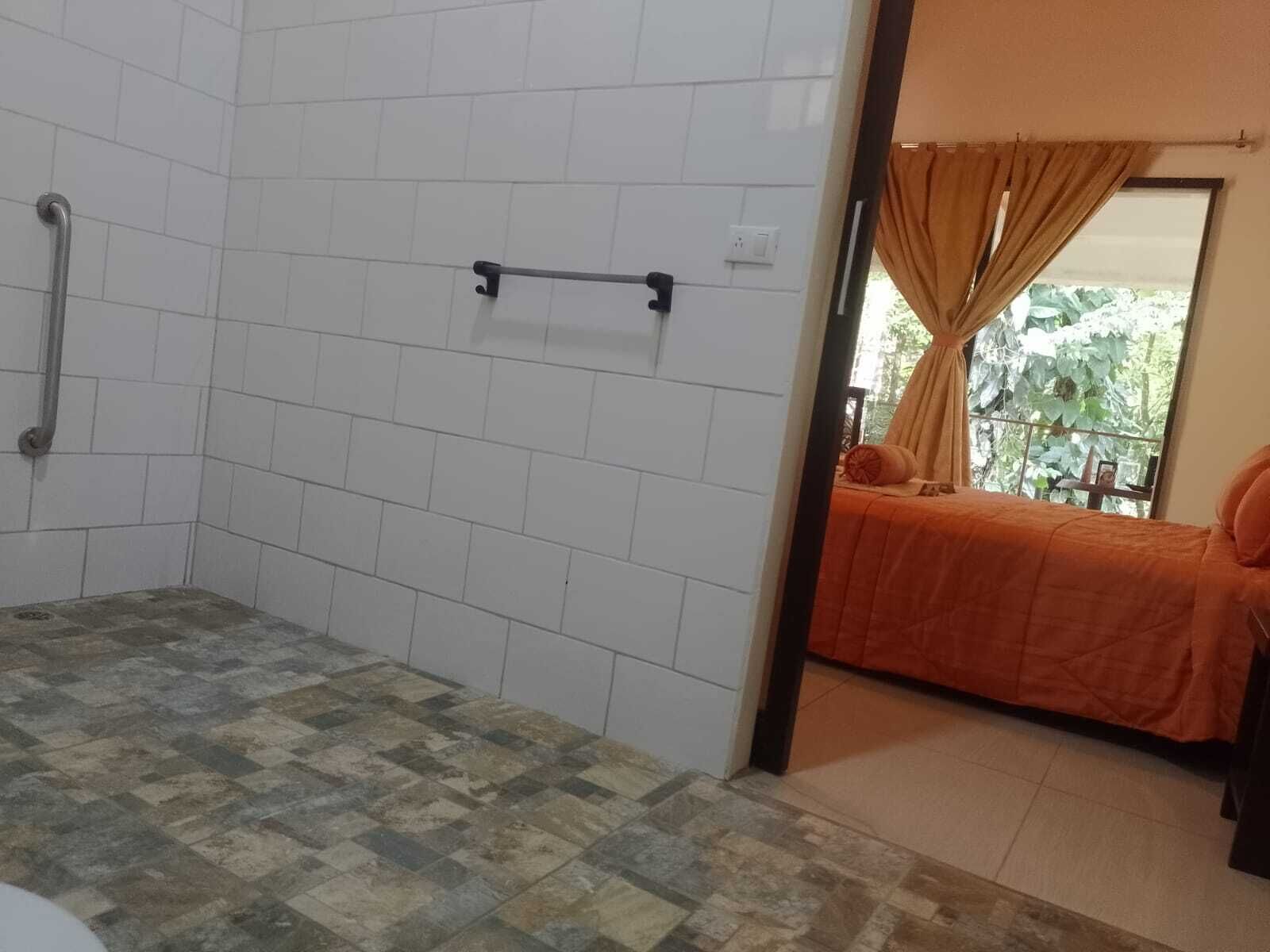 Un bagno con pareti piastrellate di bianco e pavimento a scacchi. Si nota una maniglia a sinistra e una finestra con tende a destra.