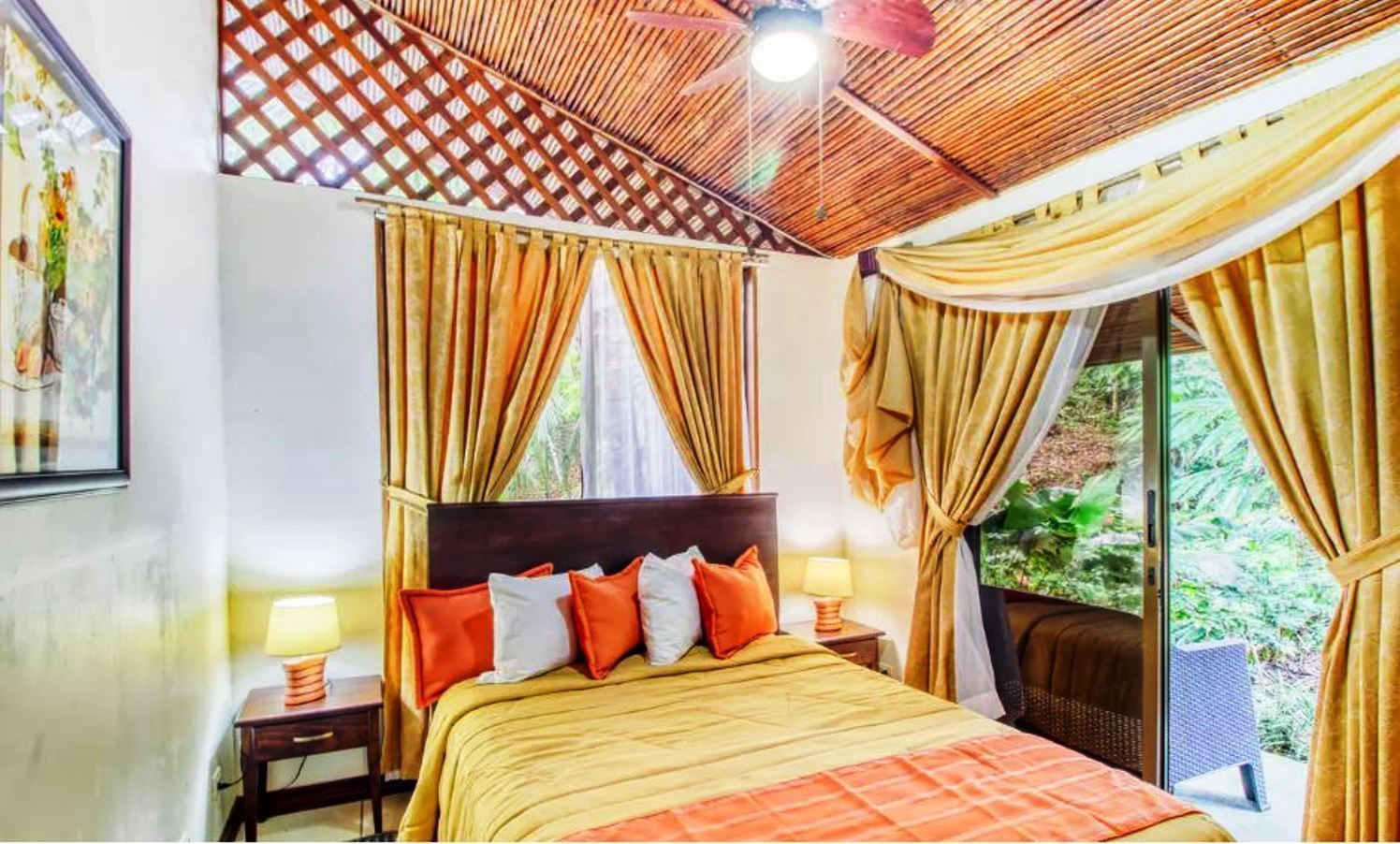 A bedroom with a bed, curtains, a headboard, a nightstand, and a window with a view of greenery.