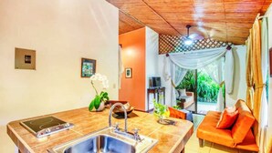 A modern kitchen with a sink, stove, and dining area. There is a sofa with orange cushions in the living area. - San Rafael Ecolodge (La Tigra)