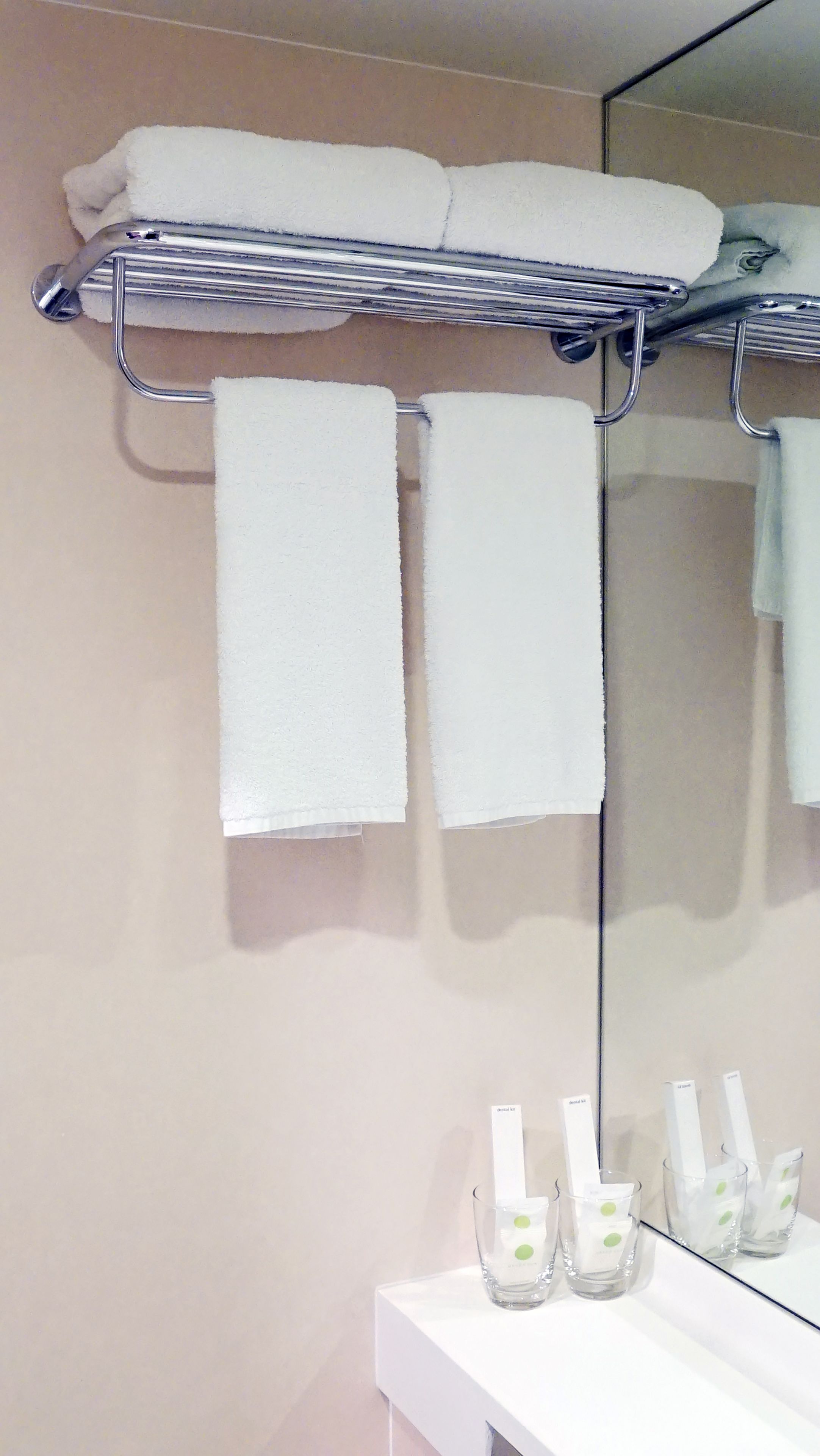 A bathroom with a towel rack holding three white towels, a mirror, and a shelf with three glass bottles.
