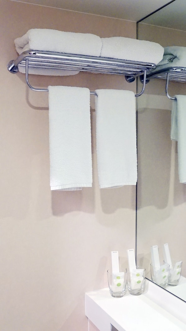 A bathroom with a towel rack holding three white towels, a mirror, and a shelf with three glass bottles. - Green Sun Hotel (Makati)