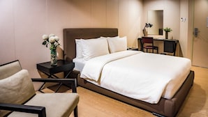 Een hotelkamer met een groot bed, een bureau met stoel, een klein tafeltje met een bloevas, en een spiegel aan de muur.