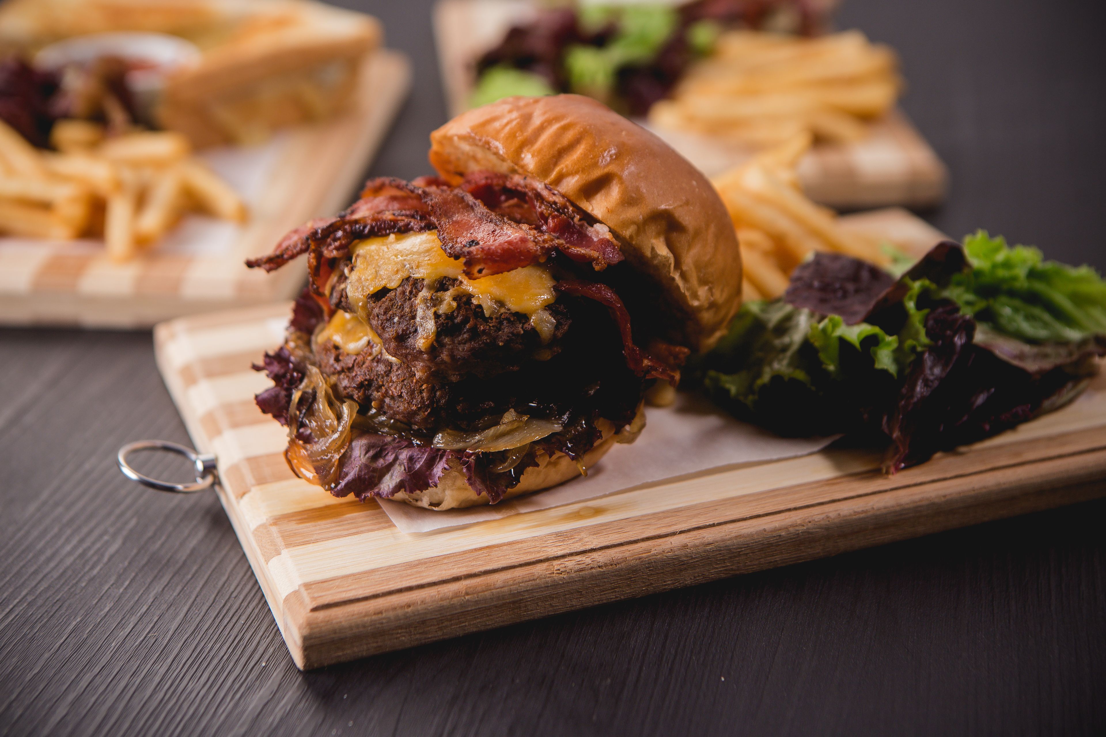 A burger with bacon, cheese, and lettuce on a wooden board.