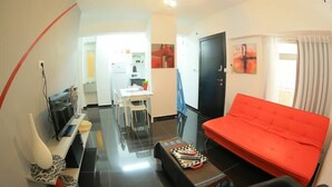 A compact living space with a red sofa, a dining table, and a kitchen area in the background. - Ben Yehuda Apartments Jerusalem (Jerusalem)