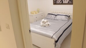 A neatly made bed with rolled towels, a bedside table with a lamp, and a framed artwork on the wall. - Ben Yehuda Apartments Jerusalem (Jerusalem)