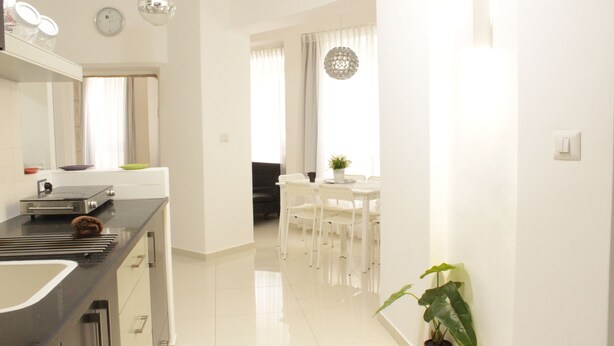 A modern kitchen with a black countertop, white cabinets, and a built-in oven. There is a dining area with a white table and chairs, and a potted plant on the side. - Ben Yehuda Apartments Jerusalem (Jerusalem)