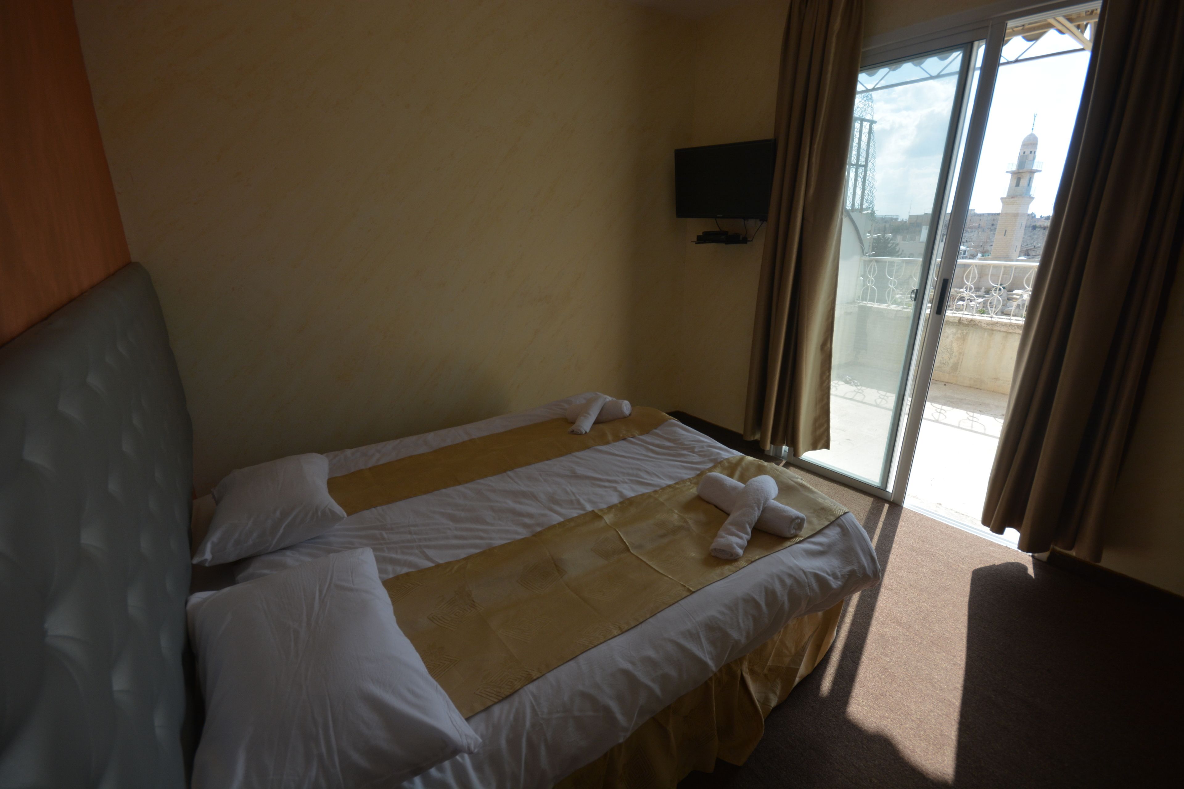 Habitación de hotel con cama, televisor montado en la pared y vista a un edificio por la ventana.