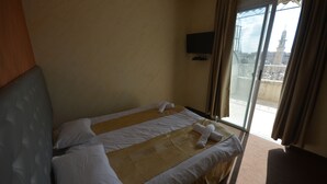 A hotel room with a bed, a TV mounted on the wall, and a view of a building through the window. - New Metropole Hotel (Jerusalem)
