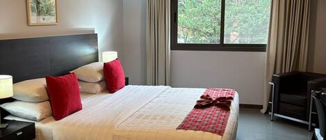 Hotelkamer met een bed, nachtkastjes, een bureau, een stoel, een raam met gordijnen, een airconditioning en een plafondlamp.