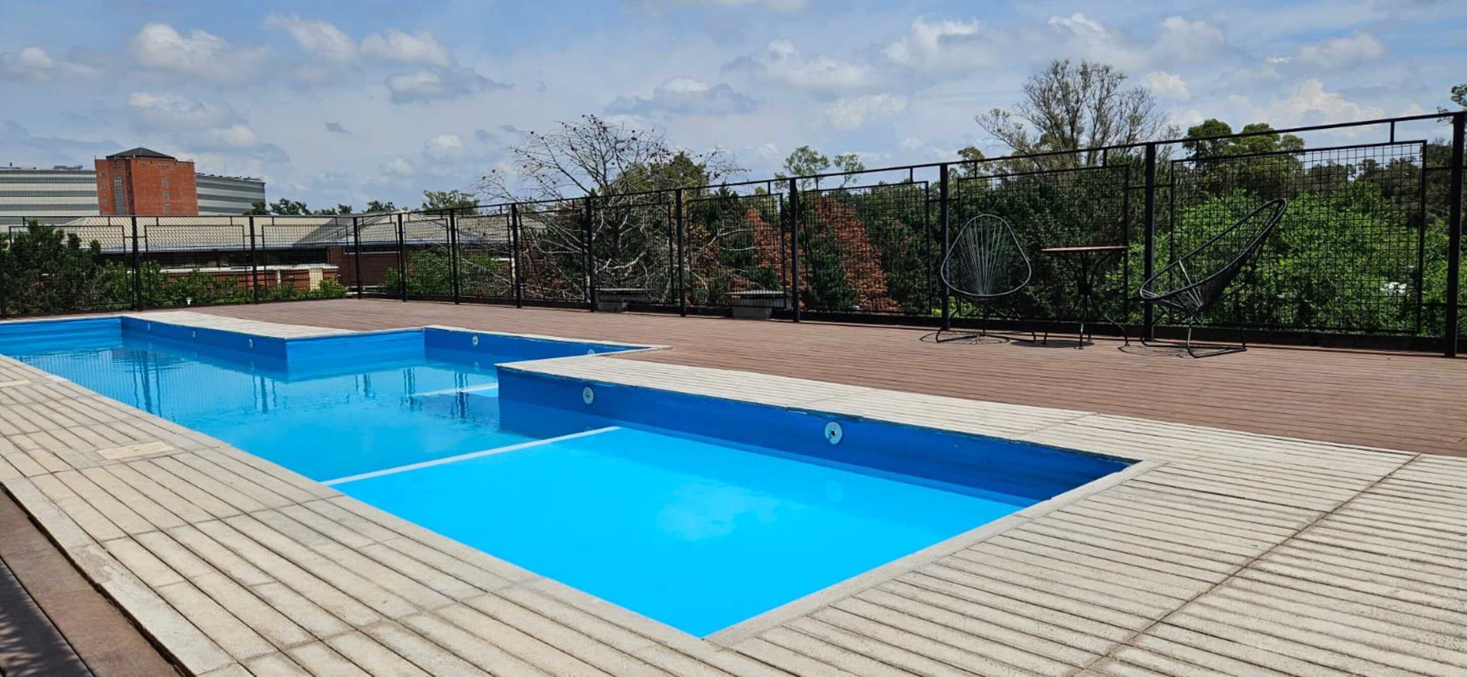 A swimming pool with a wooden deck and metal fencing.