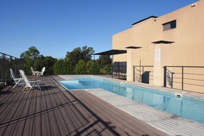 A swimming pool with a wooden deck, lounge chairs, and a building with a beige facade. - Viva Suites Pilar (La Lonja)