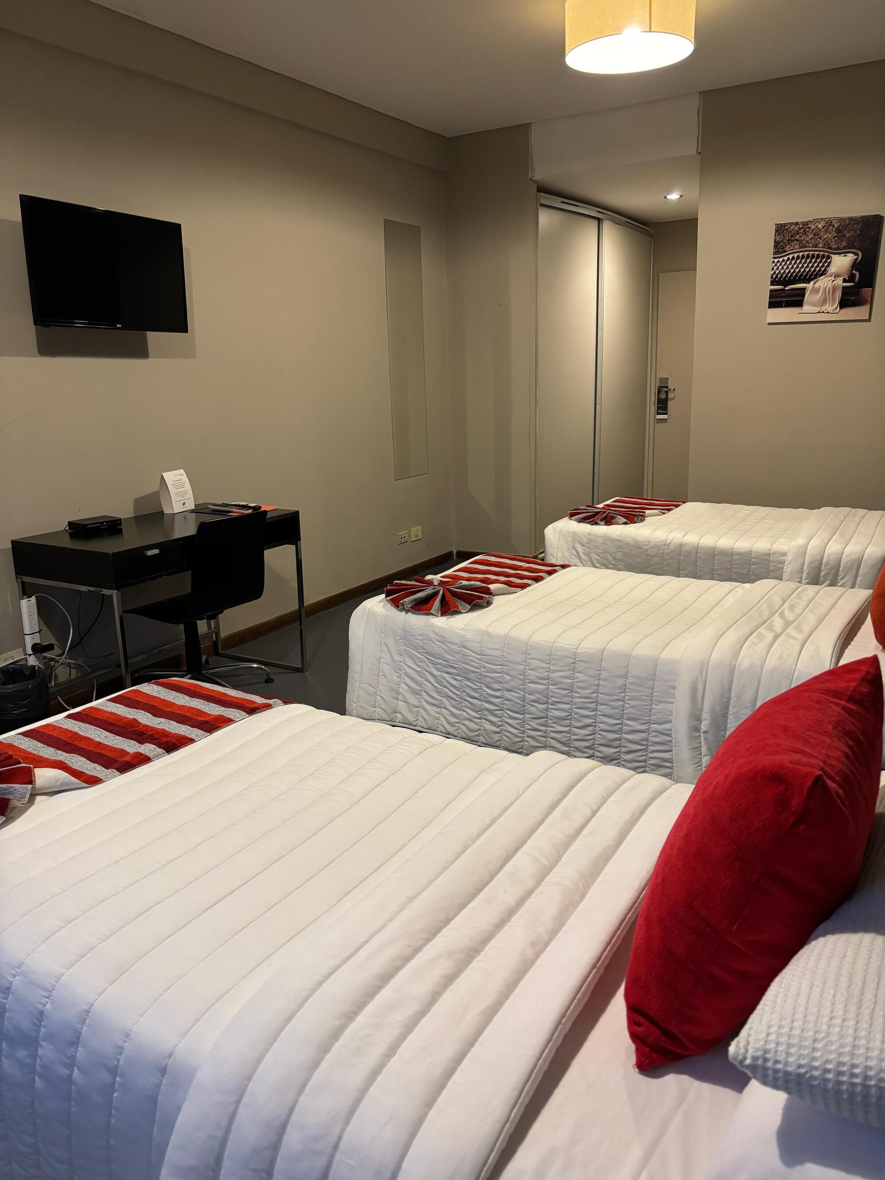 A hotel room with two beds, a desk, a flat-screen TV, and a mirror.