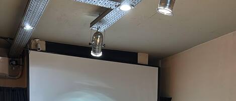 Ein Konferenzraum mit einem großen Holztisch, schwarzen Stühlen, einer Projektionsleinwand und einer Whiteboard-Tafel.