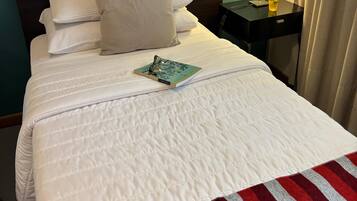 Una cama bien hecha con ropa blanca y una colcha a rayas rojas y blancas, una mesita de noche con una lámpara y un vaso de agua, y un cabecero frente a una pared verde azulado.