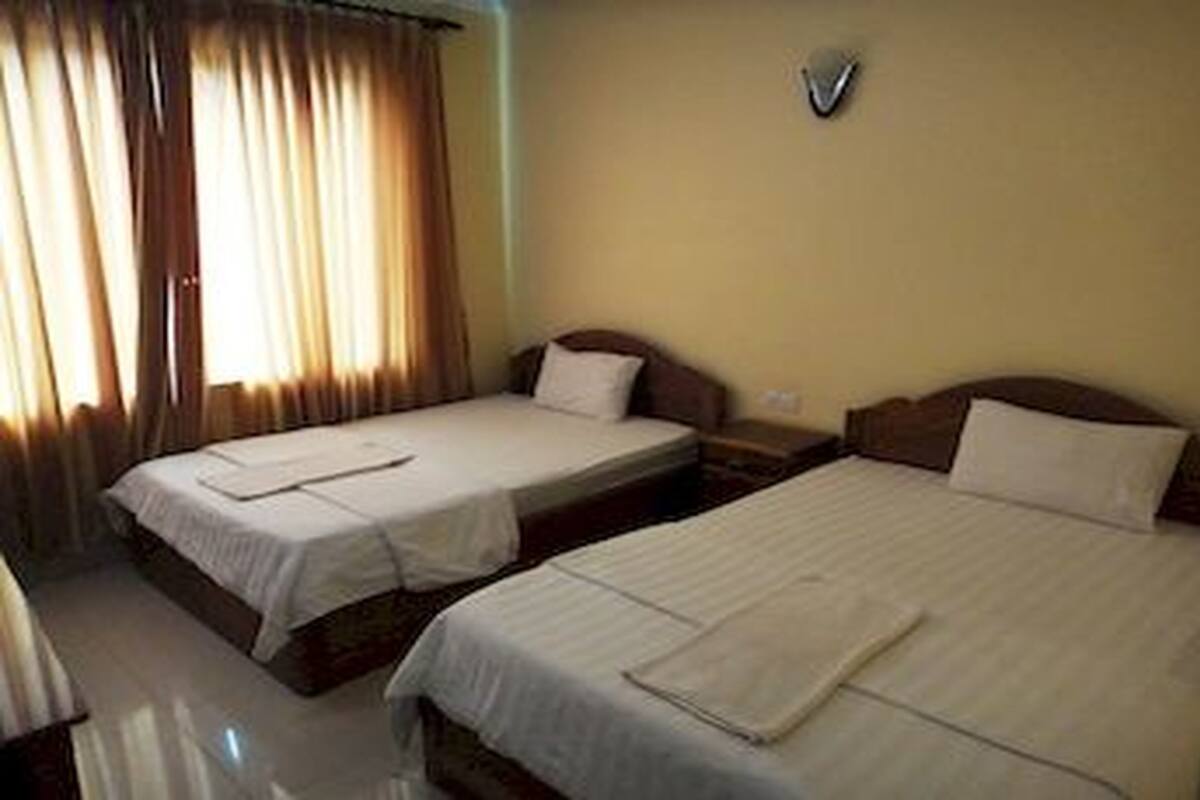 Une chambre d’hôtel avec deux lits simples, une table de chevet et une fenêtre avec des rideaux.