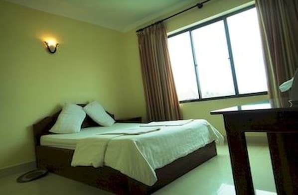 A single bed with white bedding in a room with a window and curtains.