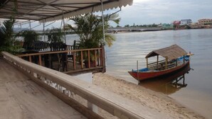 A wooden dock extending into calm water with a boat moored at the end. - The River Lodge (Kampot)