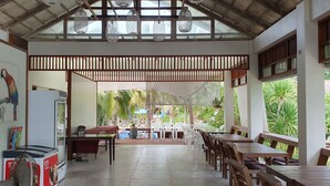 A spacious indoor area with a high ceiling, a dining area with tables and chairs, and a view of the outdoors. - Isle Beach Resort (Krabi)