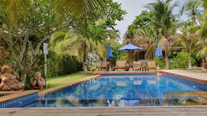 A swimming pool surrounded by palm trees and a wooden deck with lounge chairs. - Isle Beach Resort (Krabi)