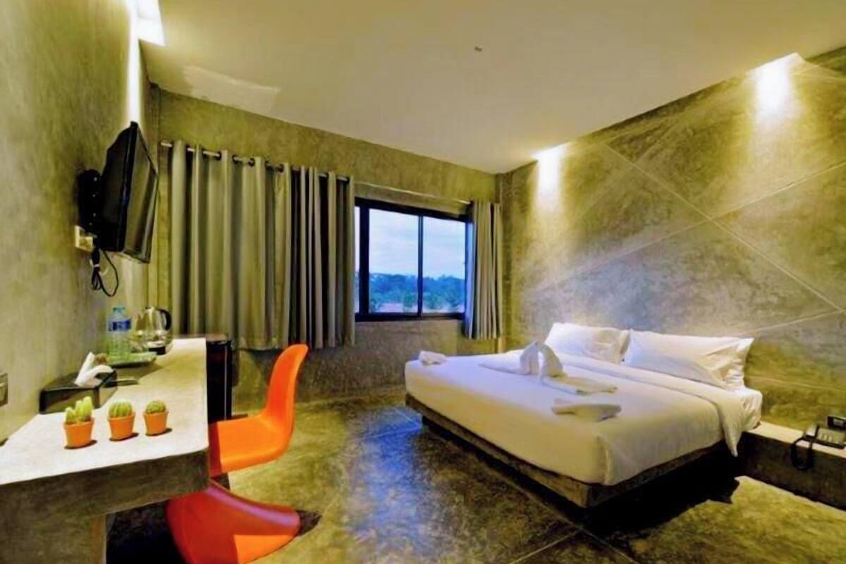 A hotel room with a bed, a desk with a chair, a TV, and a window with curtains.